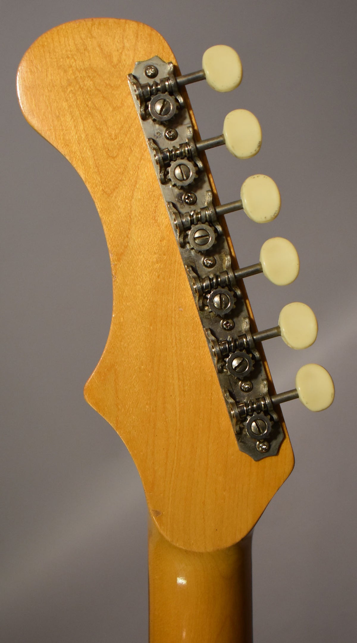 The guitar's headstock, viewed from the back, shows a light wood finish with six cream-colored tuning pegs and tarnished metal tuners.