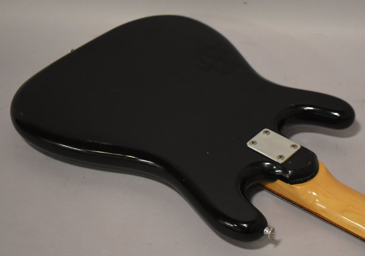 The black solidbody guitar's back is angled, showing a chrome neck plate, output jack, and light wear on the glossy finish.
