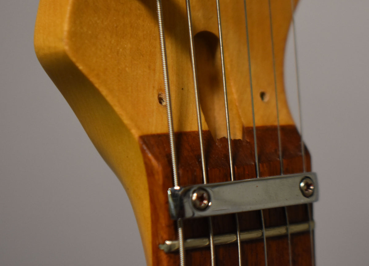 Close-up of the guitar's headstock and nut, showing the light wood finish, dark fretboard, and a chrome string retainer bar.