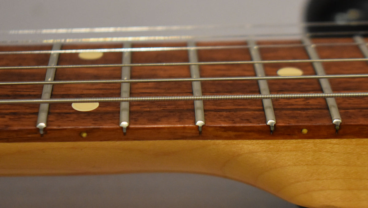 Close-up of the dark brown fretboard with round cream inlays and silver frets, showing the light wood neck below.
