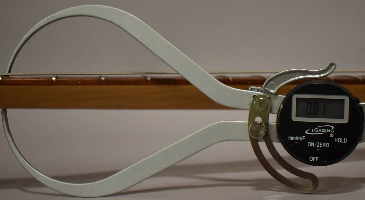 A digital caliper measures the string height above the light brown fretboard, displaying "0.81" on its black screen.