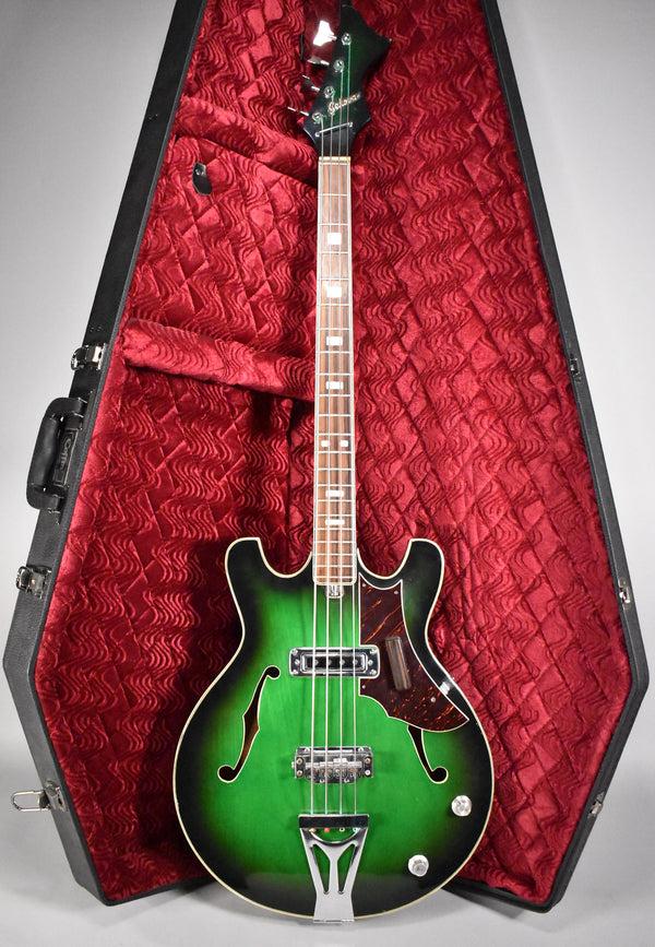 Full-length view of a green burst hollowbody bass with f-holes, white binding, two pickups, and a coffin-shaped case with red lining.