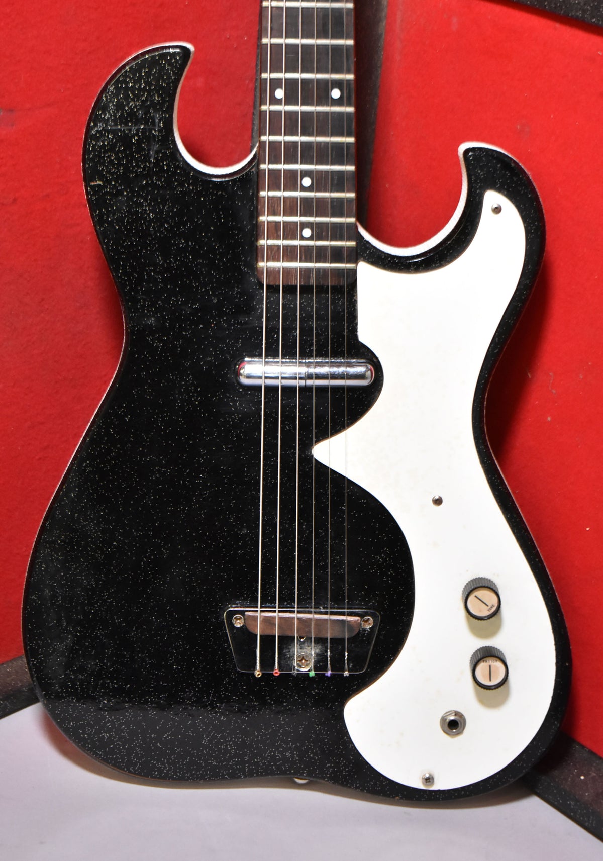 Sparkling black electric guitar with a white pickguard, two control knobs, and a chrome pickup, viewed from the upper body.