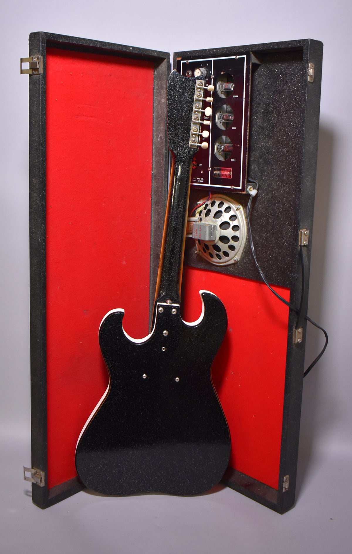 The black sparkle guitar with white binding is shown from the back, resting in its open case with a red interior and built-in amp.