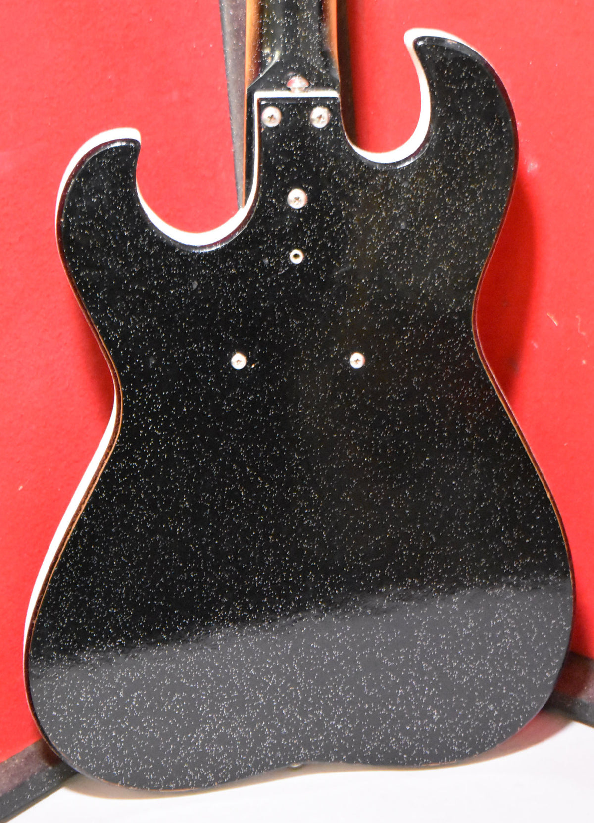 The back of a black sparkle guitar body with white binding, showing the neck plate and four visible screw holes.
