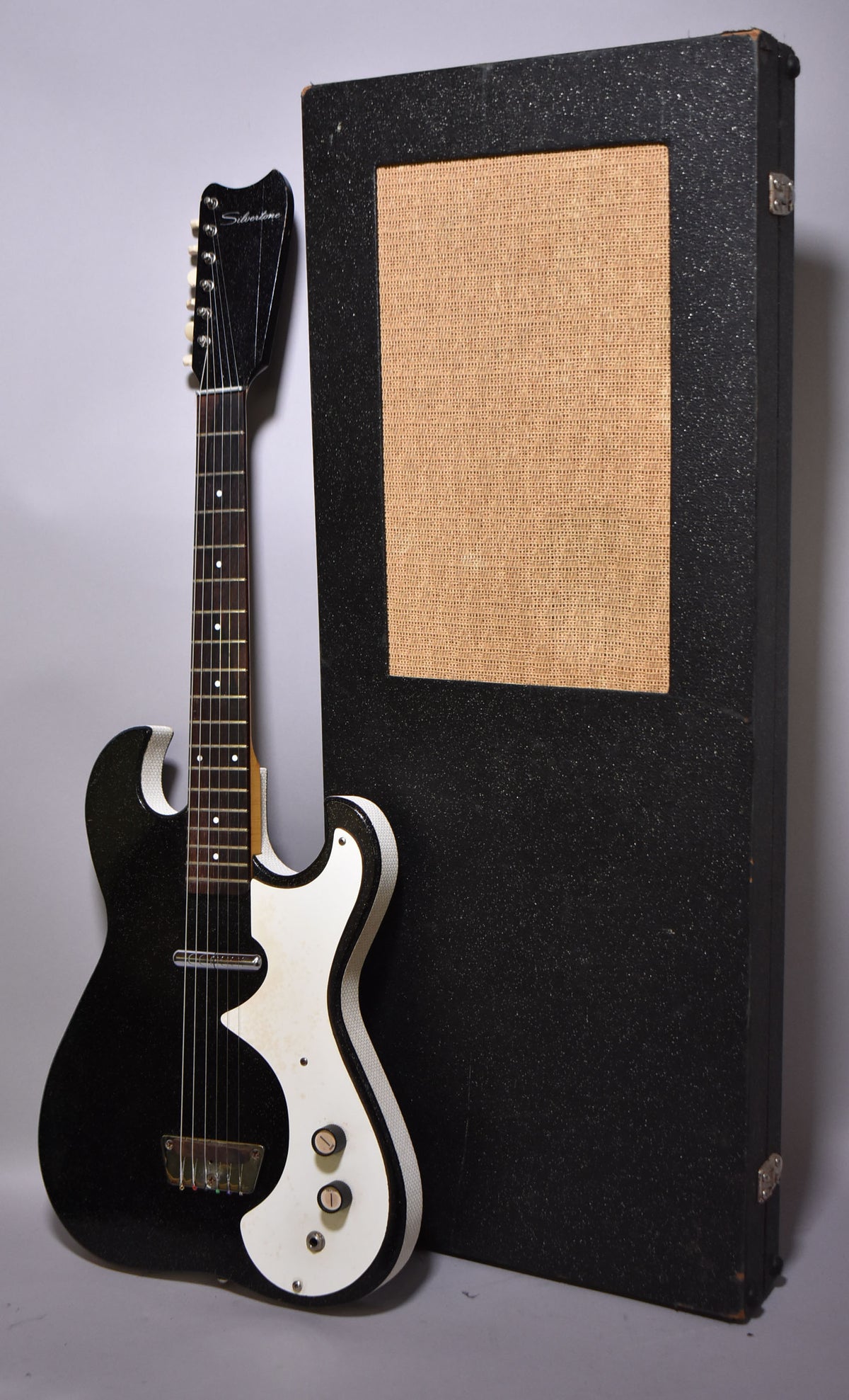 Full-length view of a black sparkle guitar with white binding and pickguard, leaning against a black case with a tan speaker grille.