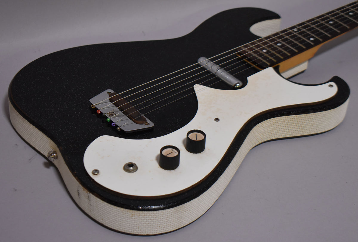 The black sparkle-finish guitar body, with white textured binding and pickguard, shows two black control knobs and wear on the lower bout.