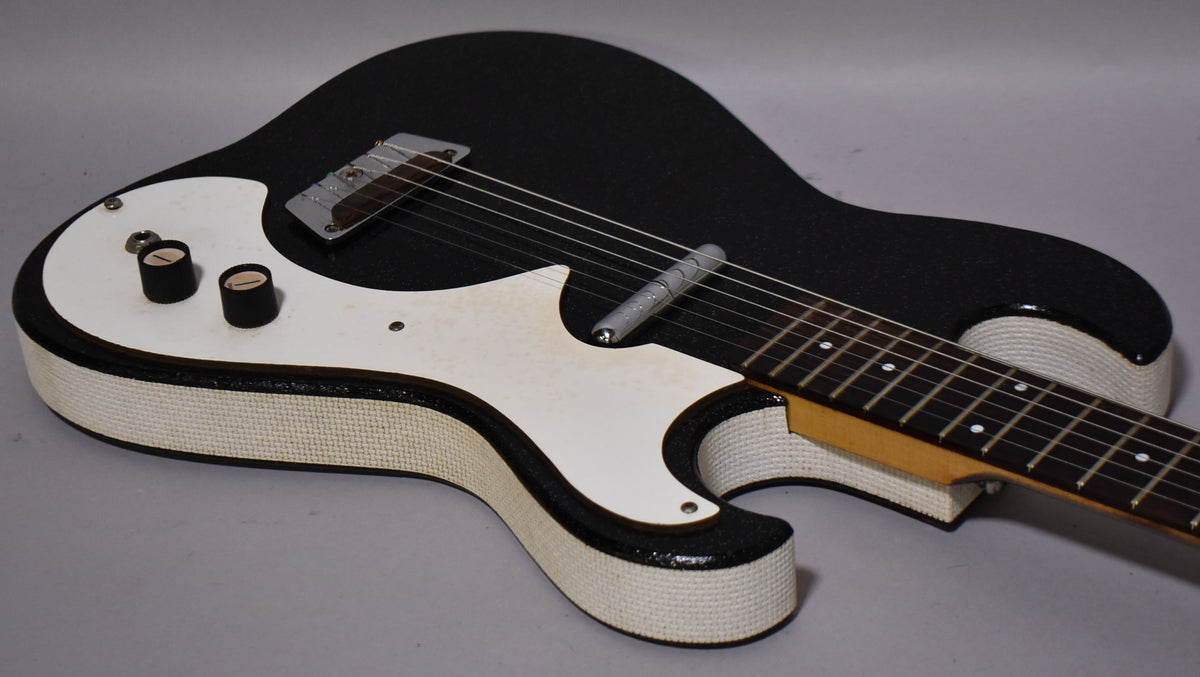 The black sparkle electric guitar is angled from the lower bout, showing its white pickguard, two black knobs, and white textured binding.