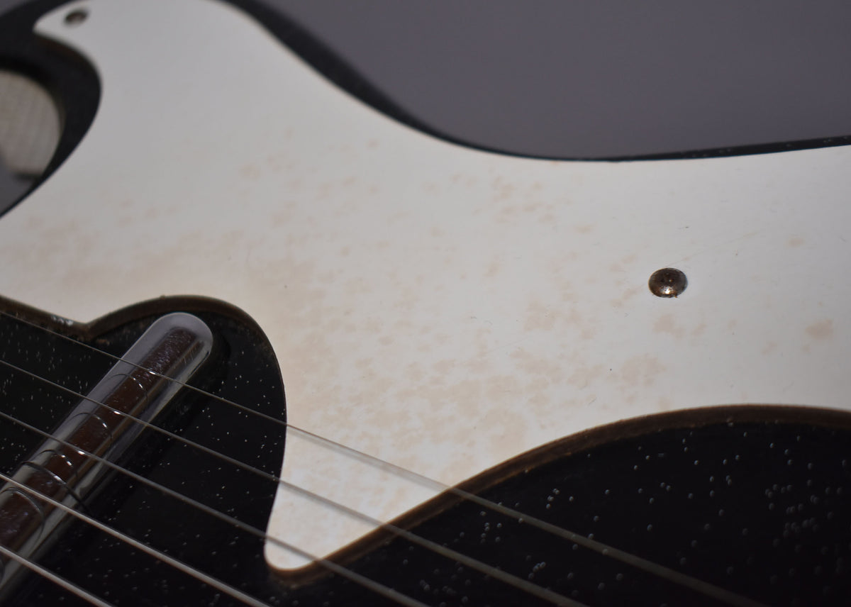 Close-up of the guitar's upper body, showing a cream pickguard with mottled aging, a single screw, and a chrome pickup.