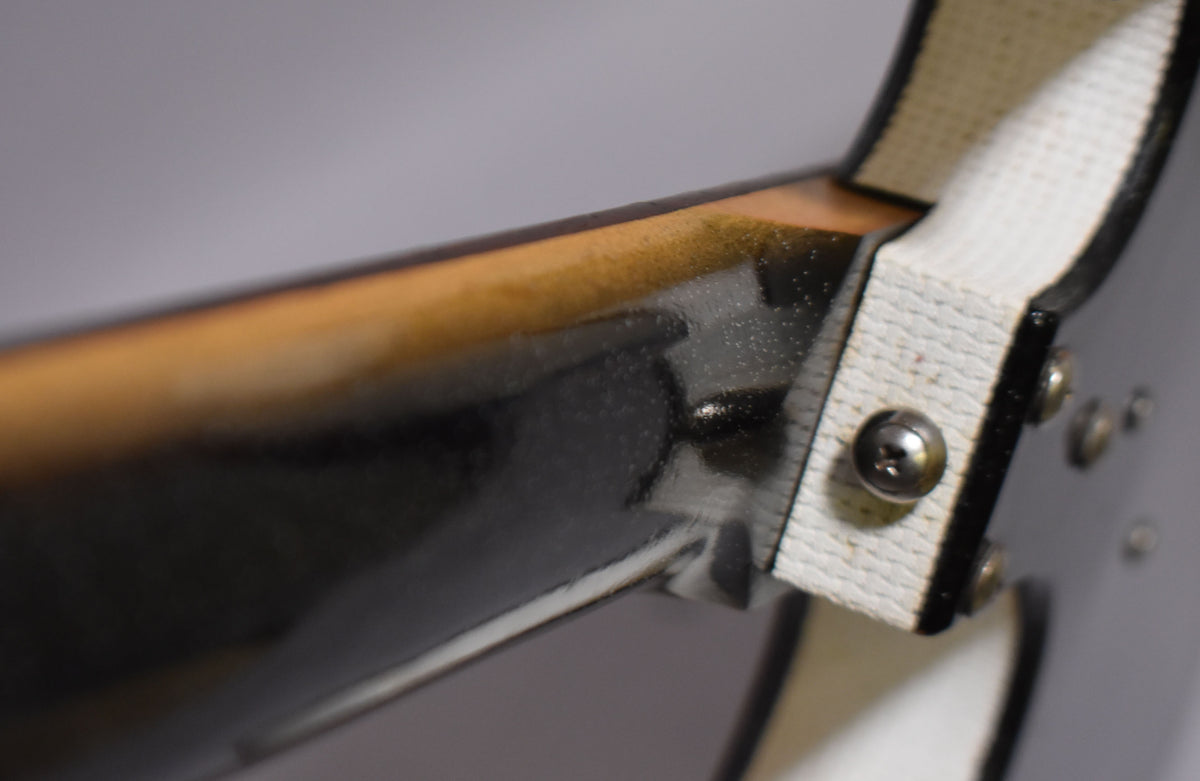 Close-up of the guitar's black neck heel and body, showing the white binding and a metal screw, with some finish checking visible.