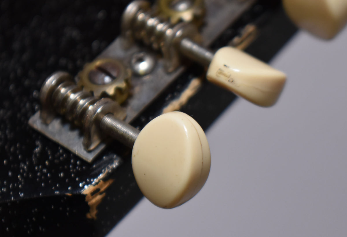 Close-up of the headstock's black finish with significant chipping, revealing wood, and two cream-colored tuning pegs.