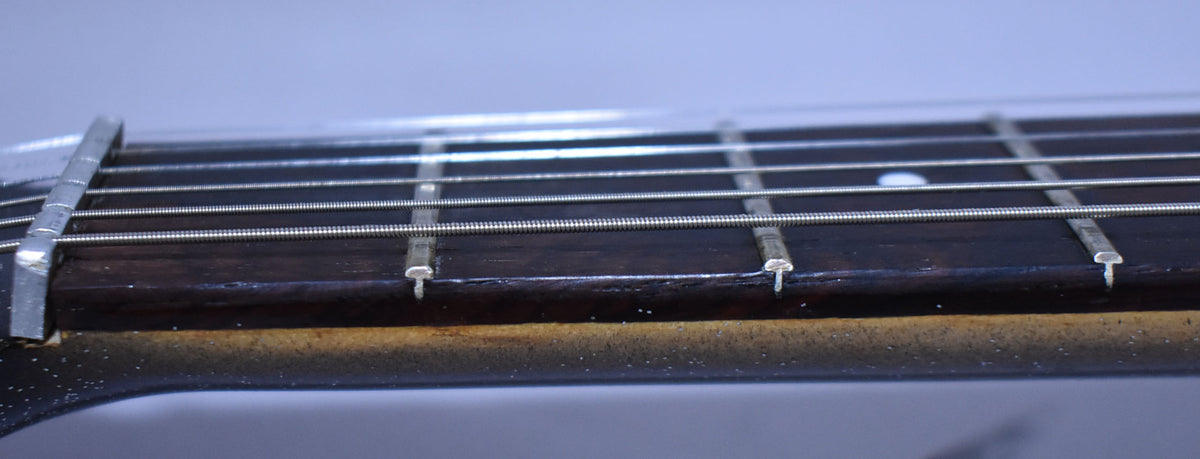 Close-up of the dark fretboard and silver frets, showing a capo clamped near the nut and a white dot inlay on the 7th fret.
