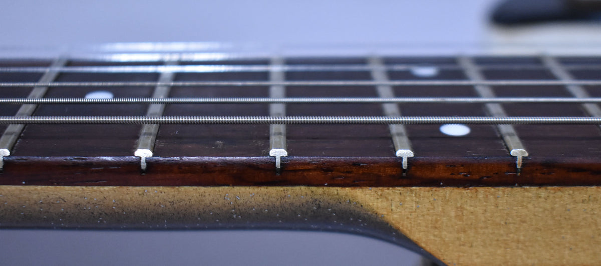 Close-up of the dark rosewood fretboard with white dot inlays, showing some wear and light checking on the neck binding.