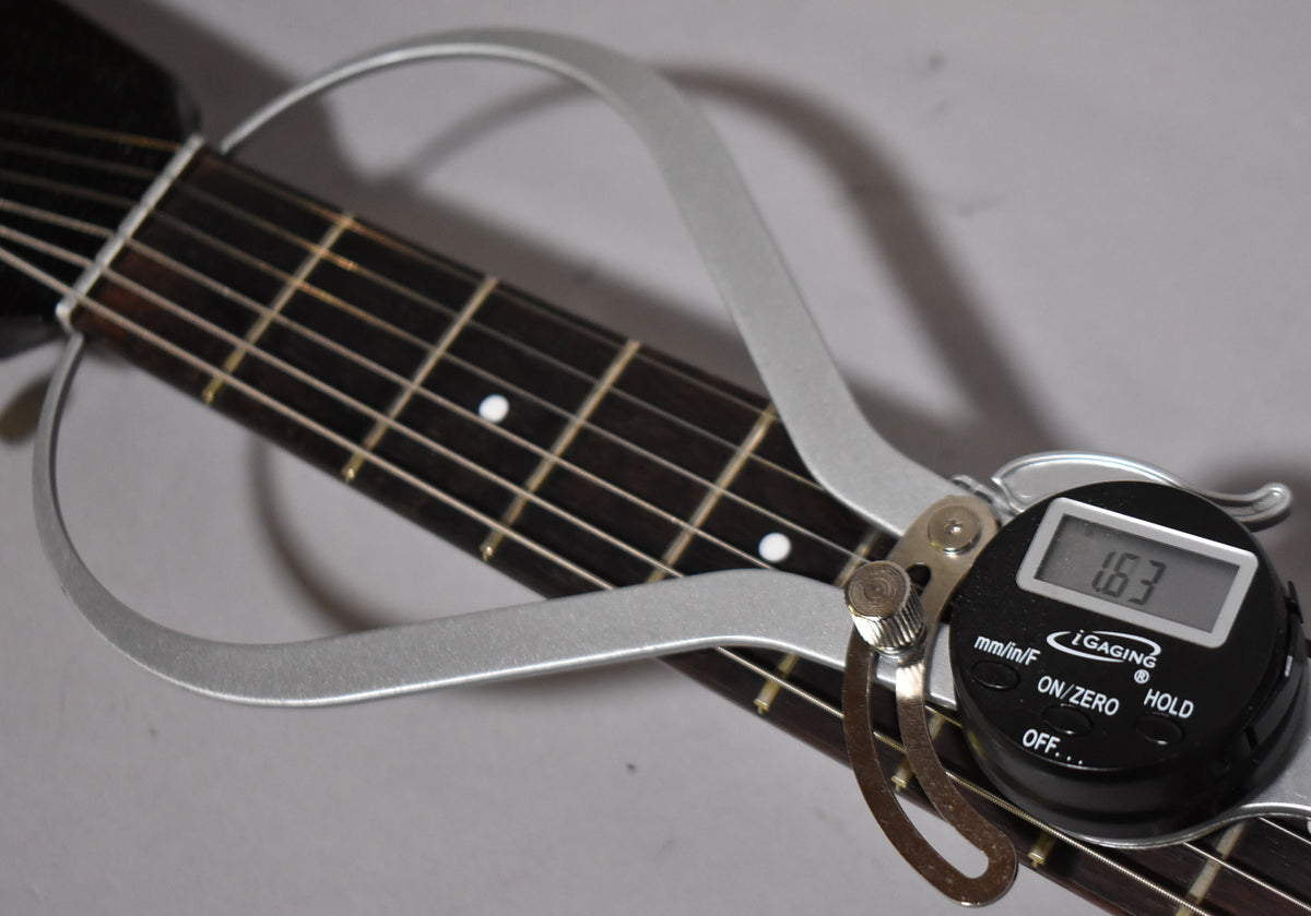 Close-up of the dark fretboard with white dot inlays, showing a silver digital caliper measuring the fret height at 1.63.