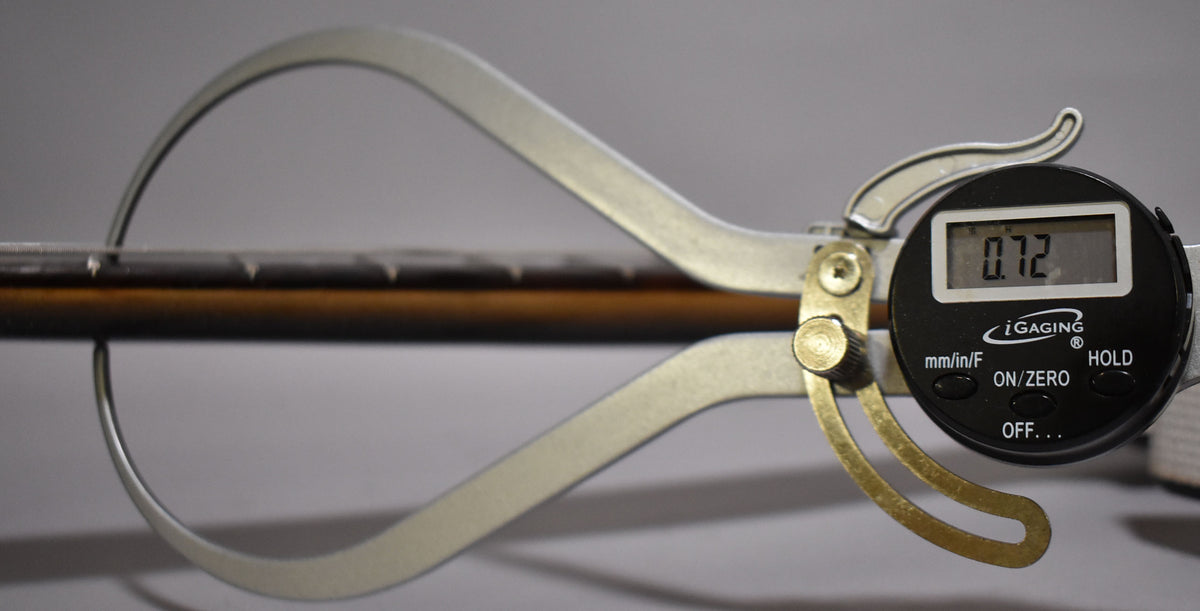 A digital caliper measures the guitar's dark brown neck, showing "0.72" on its black display.