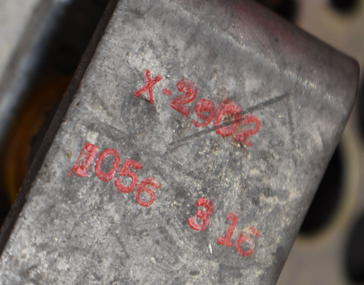 Close-up of the guitar's worn, textured metal bridge, showing red stamped numbers and letters, with some dark spots and scratches.