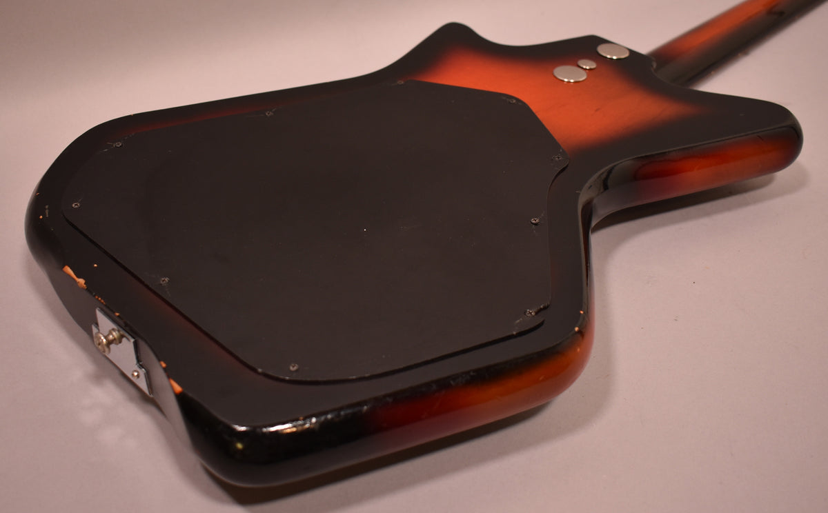 The guitar's sunburst back shows a large black control plate, two chrome strap buttons, and significant finish wear on the edges.