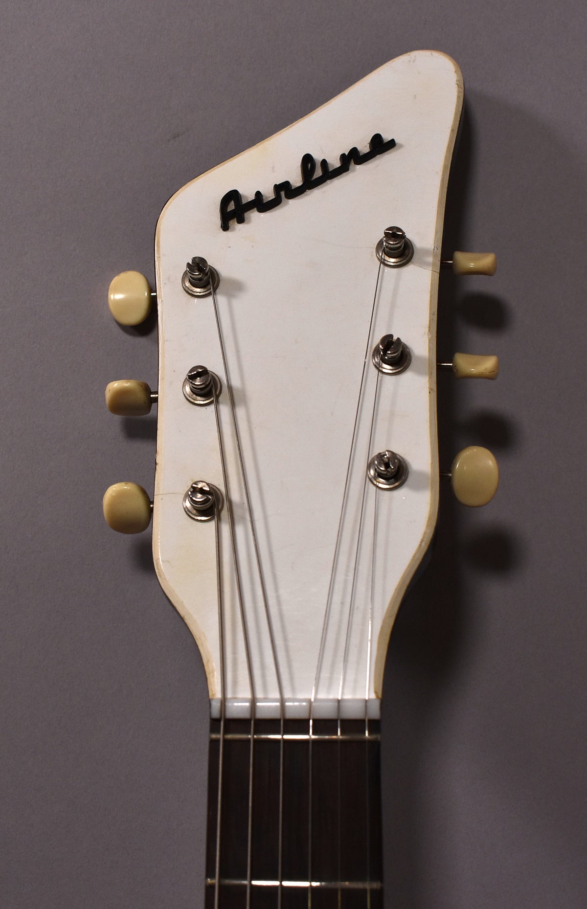 The guitar's white headstock, with six cream-colored tuning pegs, shows light wear and a black script logo.