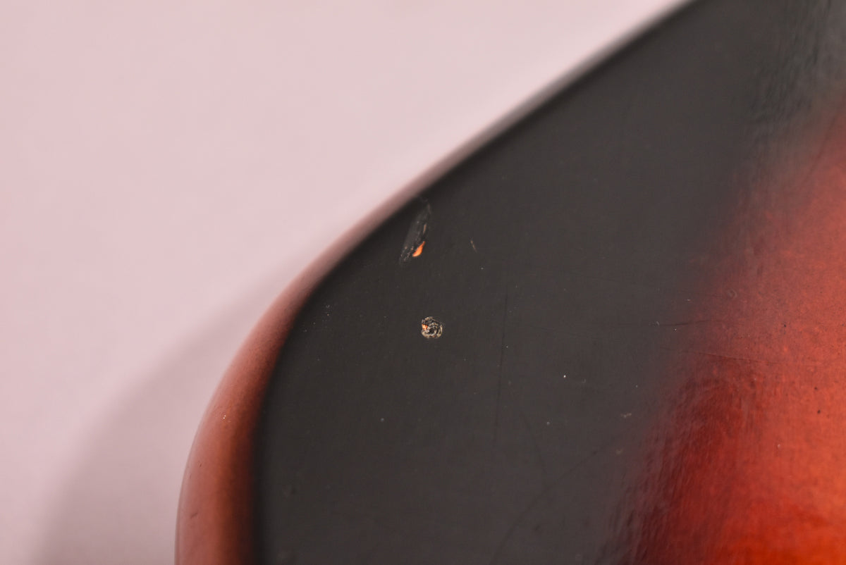 Close-up of the sunburst body, showing a few small chips in the black finish revealing orange beneath, and light surface scratches.