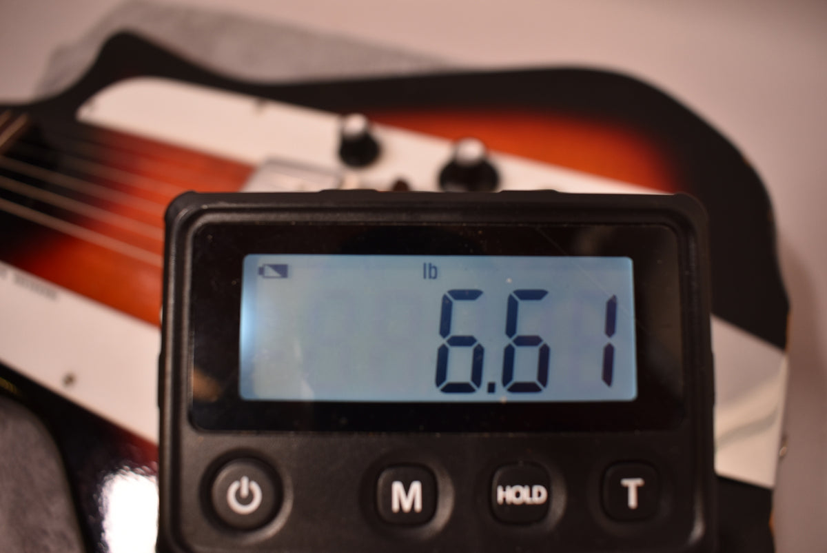 A digital scale displays "6.61 lb" in the foreground, with the guitar's sunburst body and controls blurred behind it.