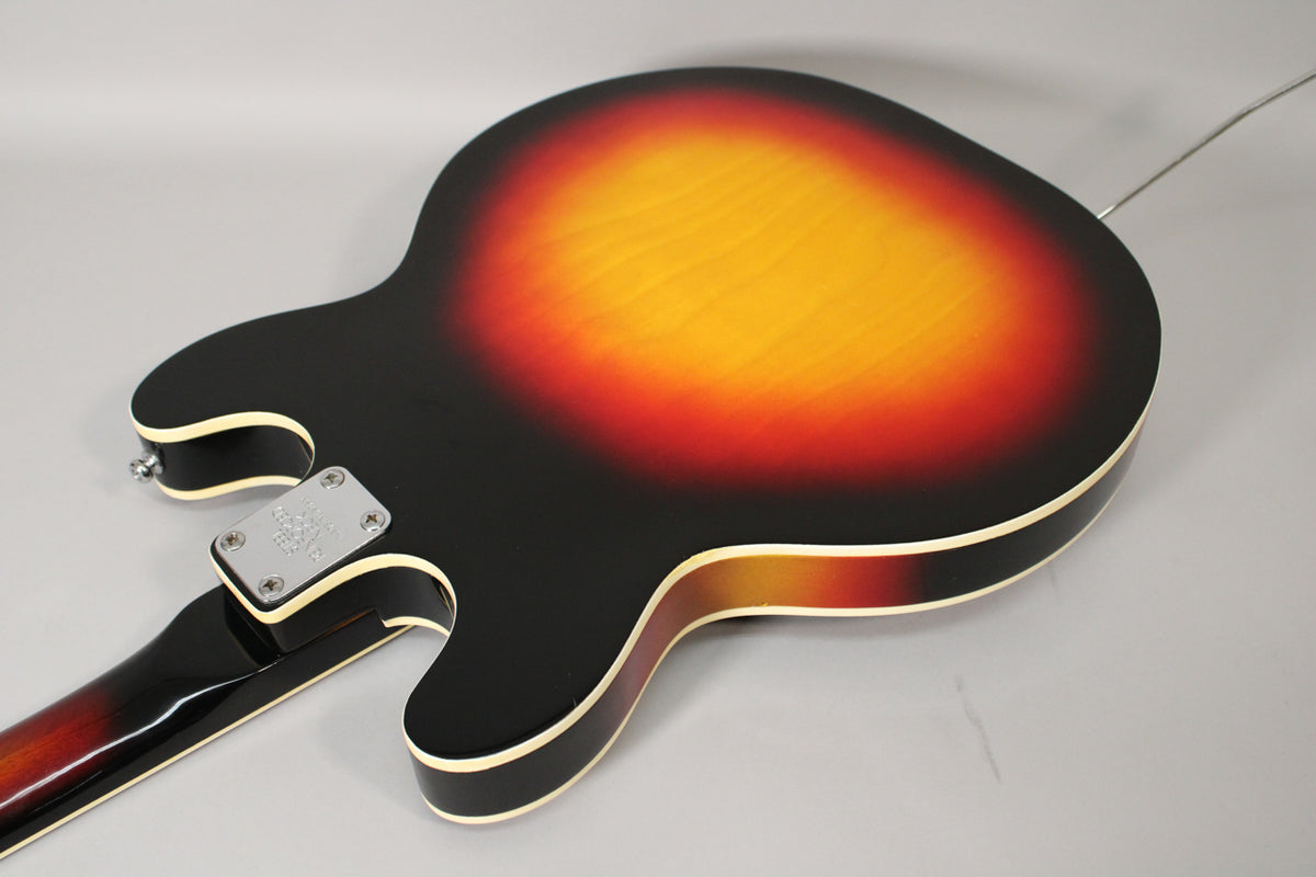 The back of a sunburst hollowbody guitar, showing the neck joint, chrome neck plate, and a thin white binding around the body.