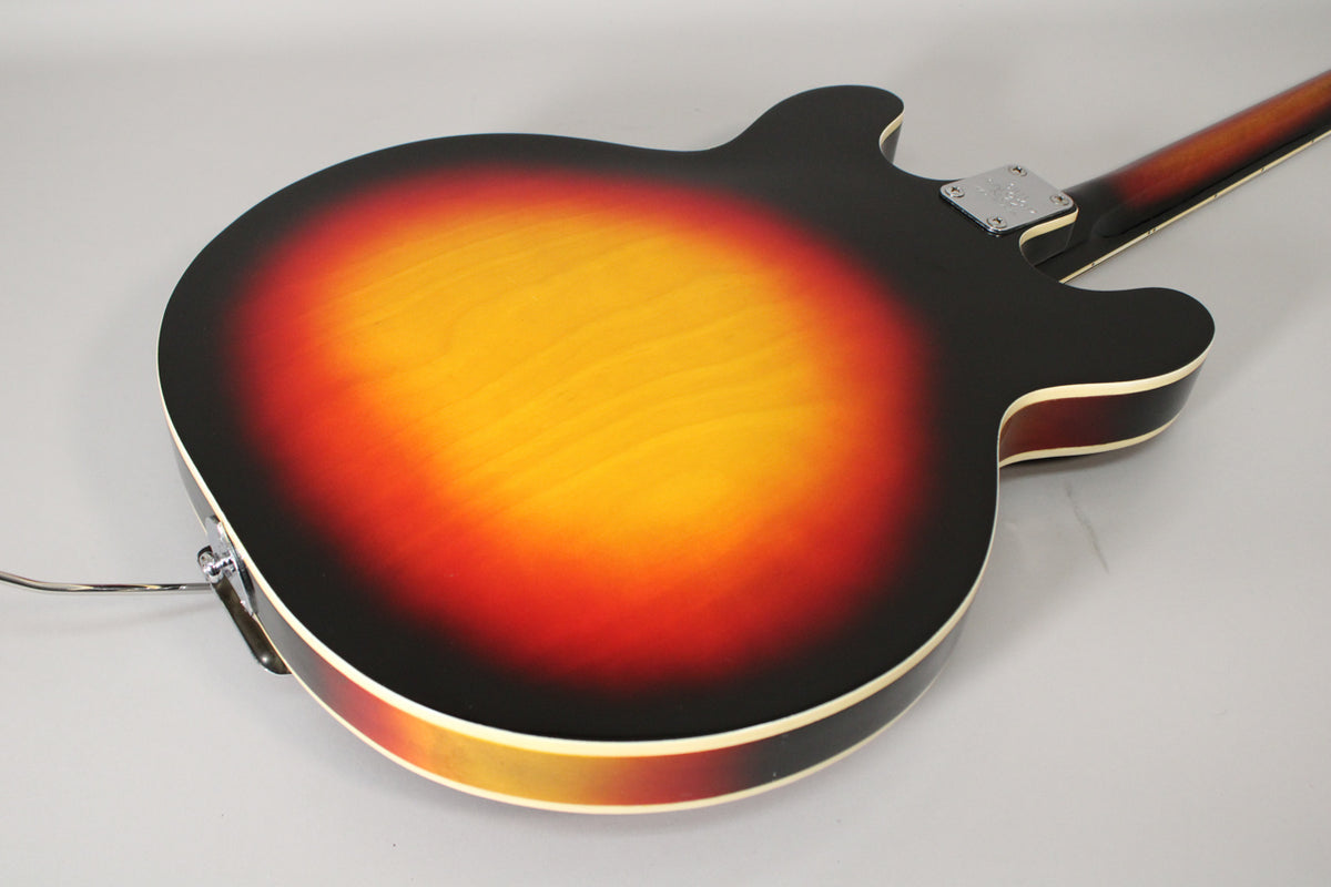 The back of a sunburst hollowbody electric guitar, showing the neck joint, output jack, and light finish wear.