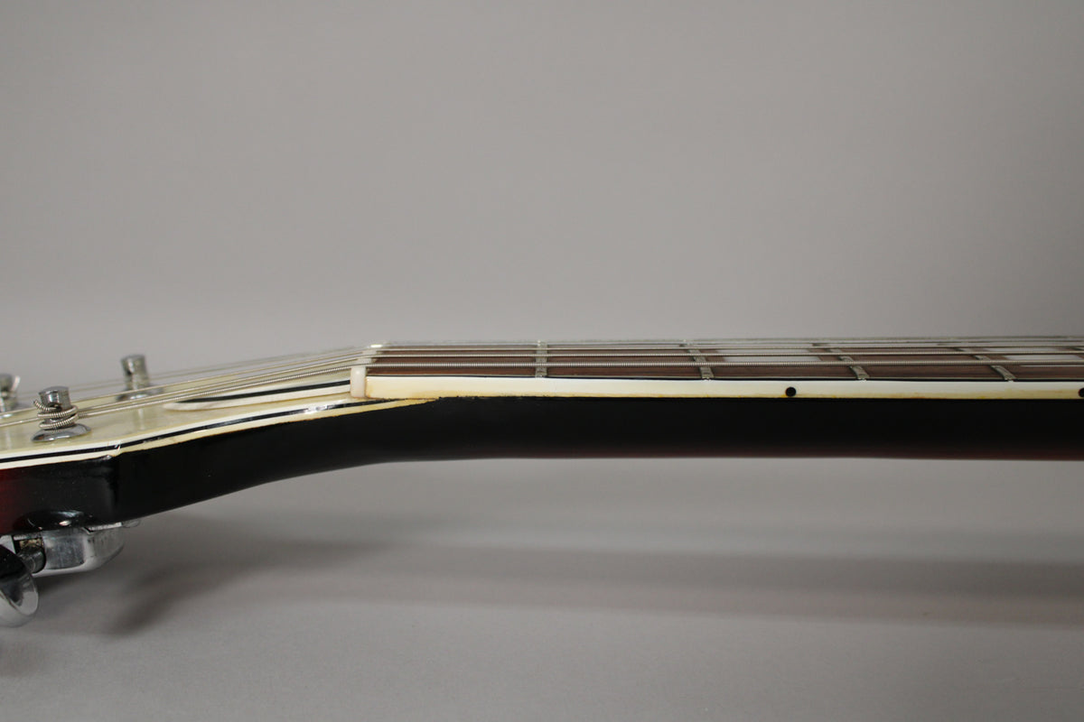 Side view of the guitar neck, showing the dark brown neck, cream binding, fretboard with dot inlays, and the nut.