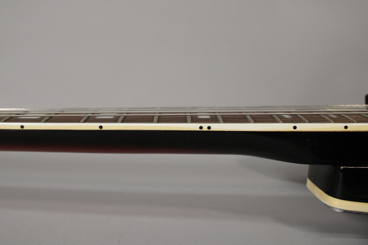 The guitar's neck, viewed from the bass side, shows a dark fretboard with rectangular inlays and cream binding.