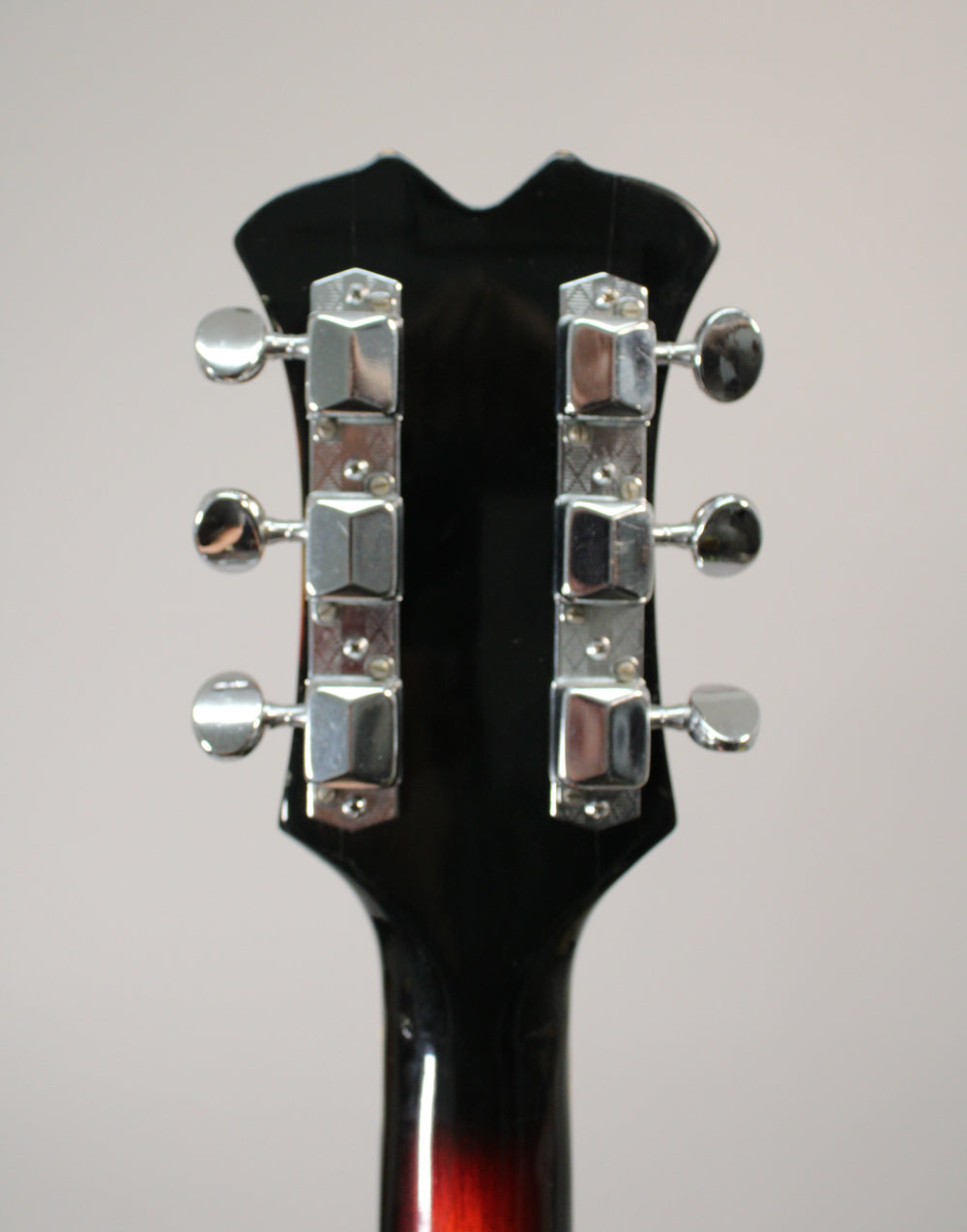 The back of a guitar headstock, black with a sunburst neck, showing six chrome tuners with rectangular housings.