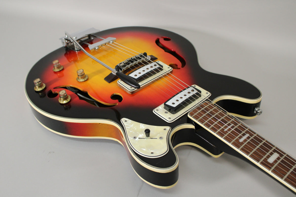 A sunburst hollowbody electric guitar with f-holes, four gold knobs, two white humbuckers, and a pearloid switch plate.