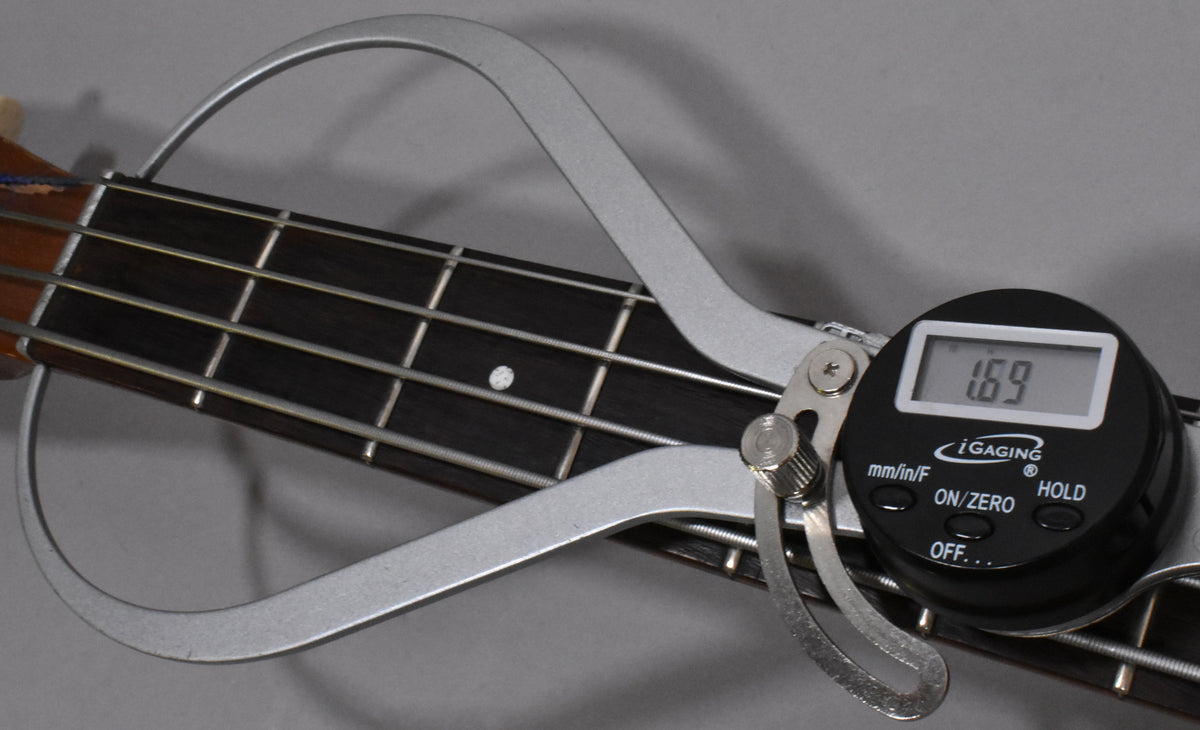 Close-up of the bass's dark fretboard with four strings, showing a digital gauge measuring 1.69mm of string action.