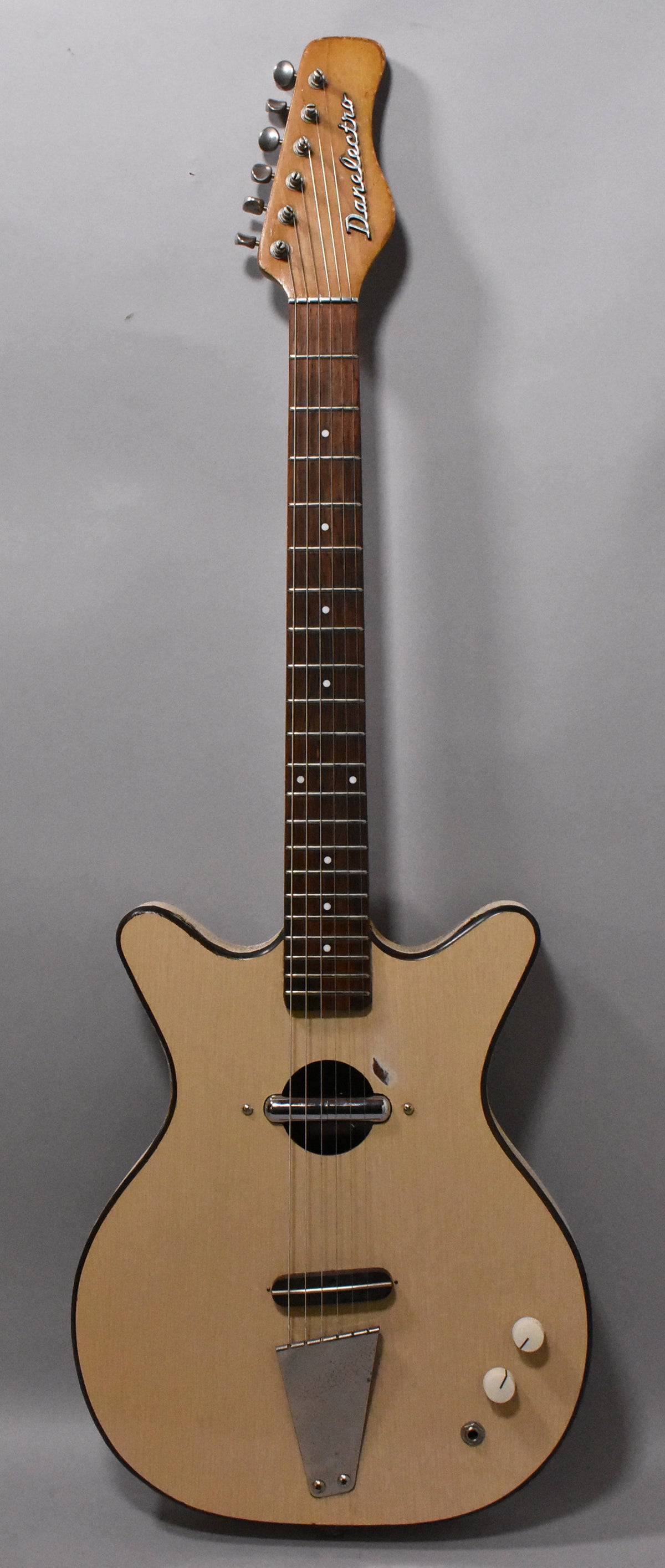 Full-length view of a light natural finish electric guitar with a dark fretboard, a single round soundhole, and two white control knobs.
