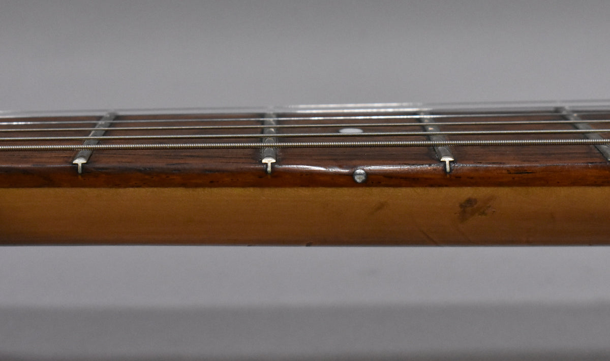 Close-up of the guitar's dark brown fretboard and light brown neck, showing frets, strings, and a side dot marker, with some wear.