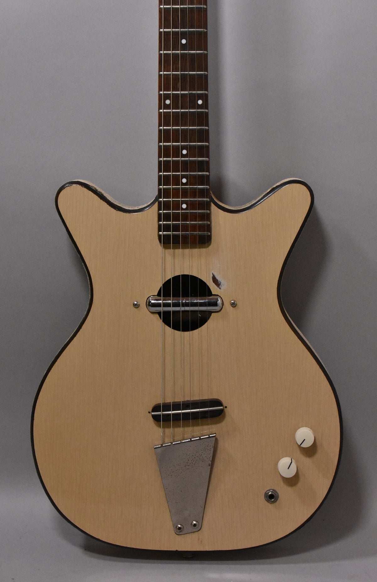 Full-frame, front view of a natural finish guitar with a single pickup, two white knobs, and a worn metal tailpiece.