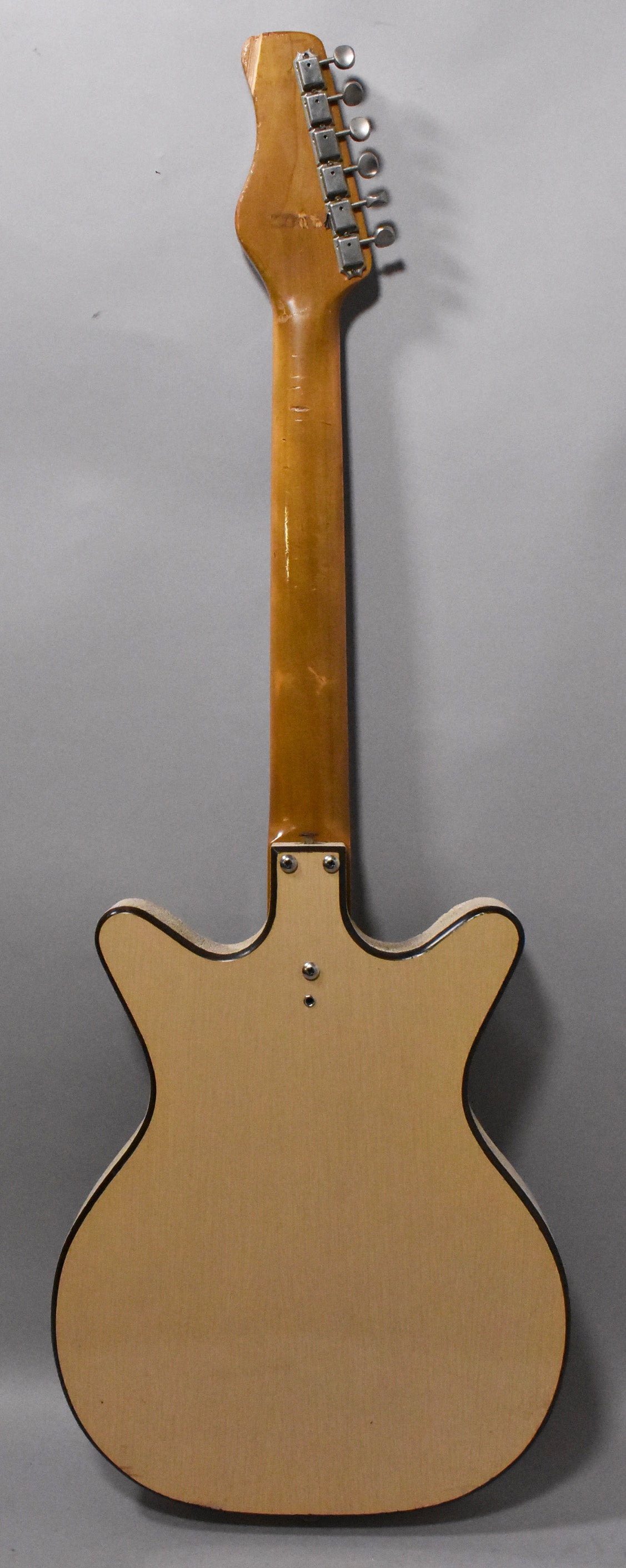 The back of the natural finish guitar, showing the light-colored body with dark binding, a bolt-on neck, and six inline tuners.