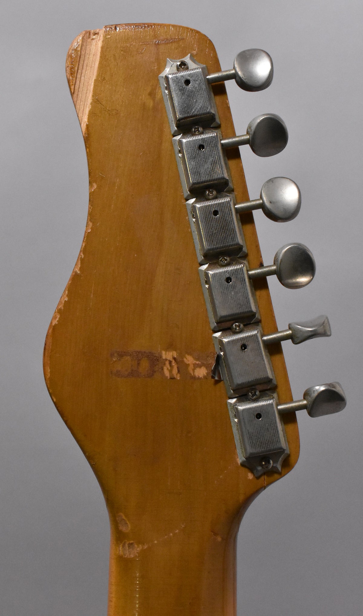 Rear view of the guitar's headstock, showing six metal tuners, a natural finish, and significant wear and chipping on the wood.