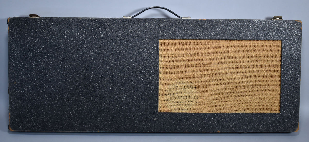 Top-down view of the black textured case with a tan woven speaker grille, a black handle, and worn corners.