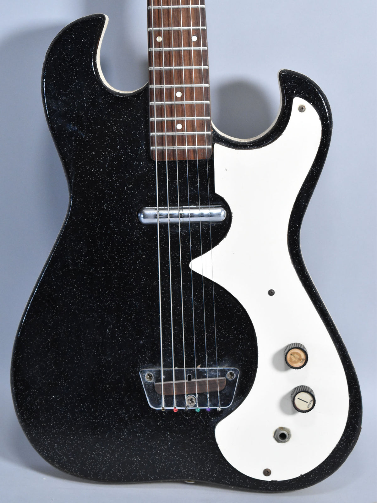 The black sparkle finish guitar body, with a white pickguard, shows a single pickup, two control knobs, and a clear bridge cover.