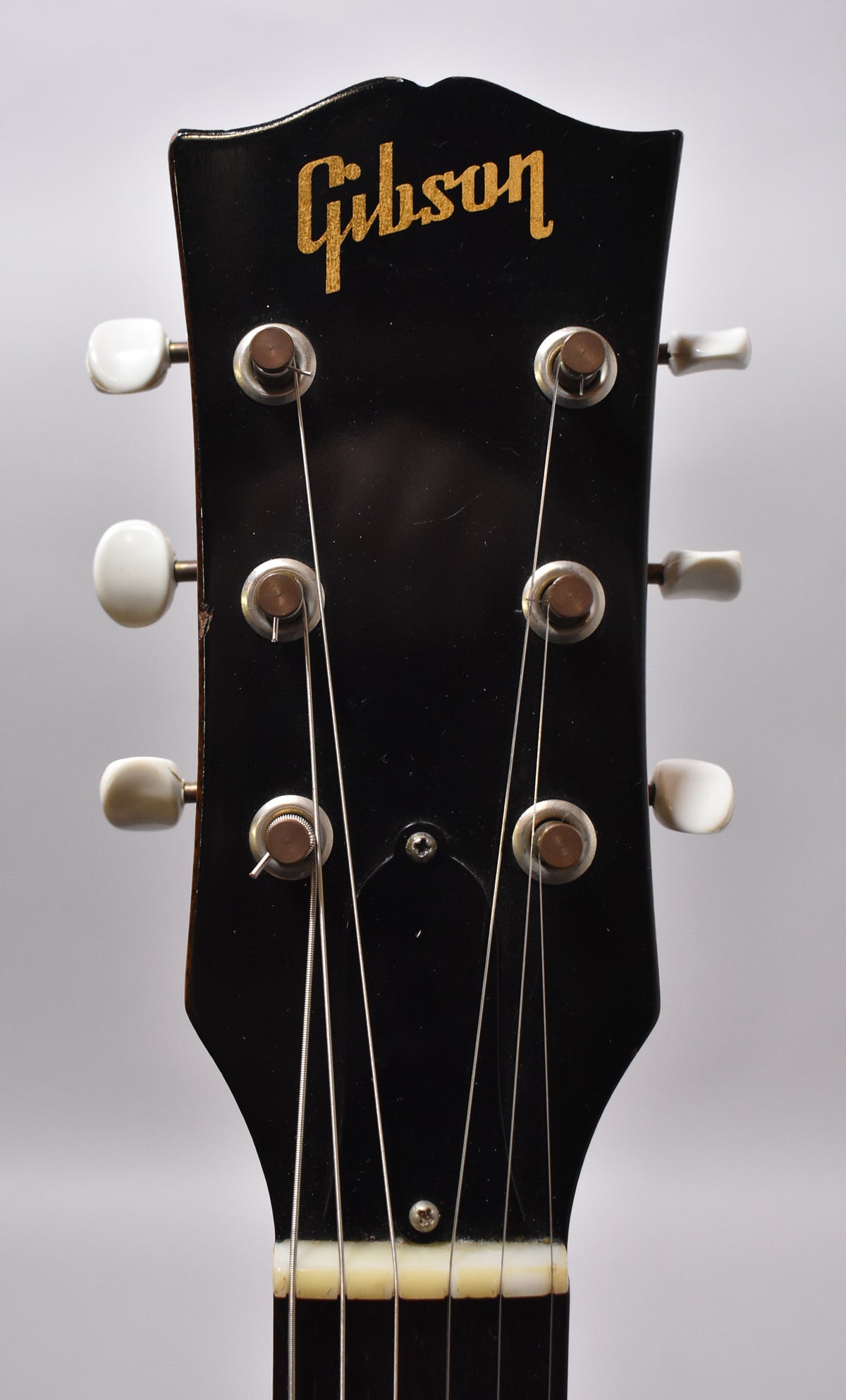 The black headstock, with gold lettering and six white tuning pegs, shows light wear and some finish checking.