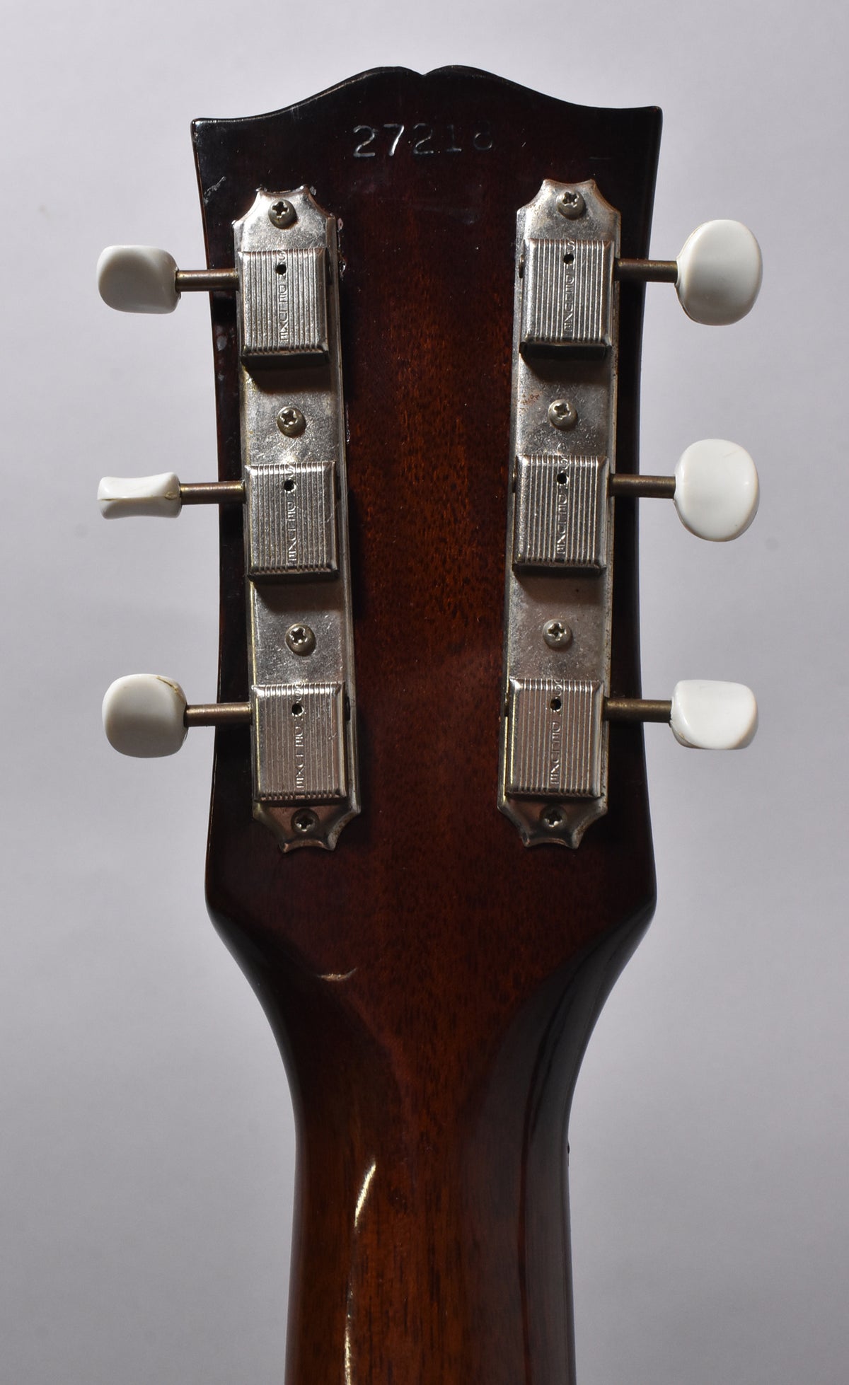 Rear view of the guitar's dark brown headstock and neck, showing six white tuning pegs and two chrome tuners with light wear.