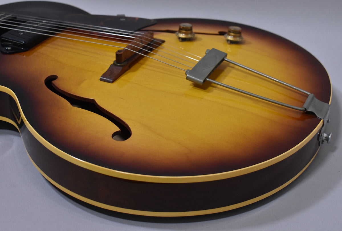 Close-up of the sunburst archtop body, showing the f-hole, wooden bridge, metal trapeze tailpiece, and two gold-capped control knobs.