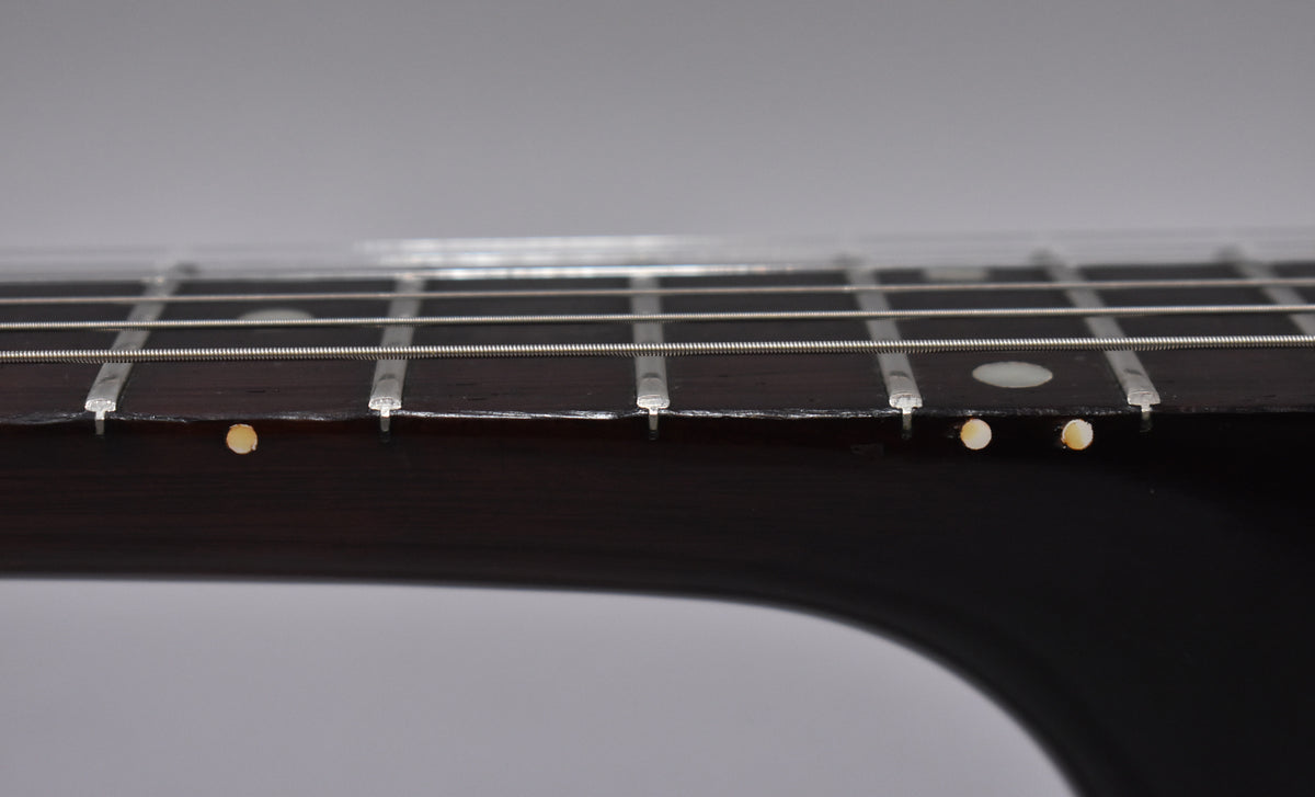 Close-up of the dark rosewood fretboard, showing frets, strings, and side dot markers with some wear and discoloration.