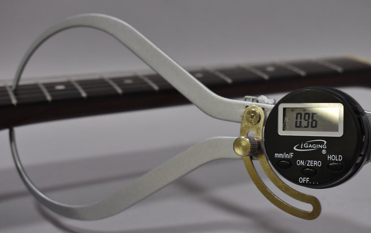 A digital caliper measures the guitar's dark fretboard, showing a reading of 0.96 on its black display.