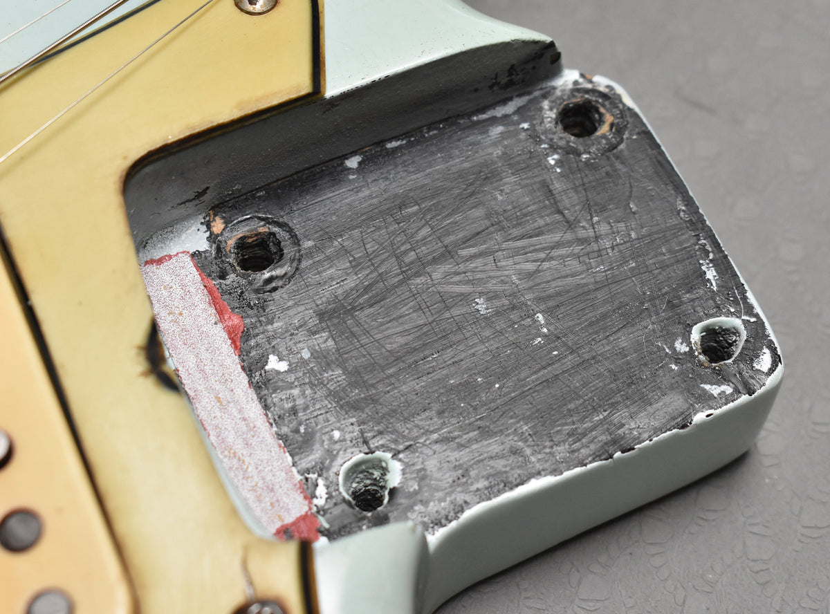 Close-up of the neck pocket, showing the aged sonic blue finish, exposed wood, and four screw holes.