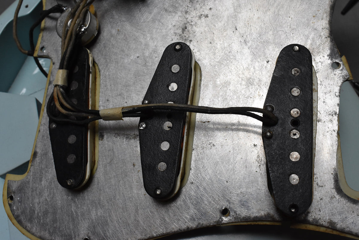 Close-up of three aged black single-coil pickups with exposed pole pieces, wired together over a worn metal shielding plate.