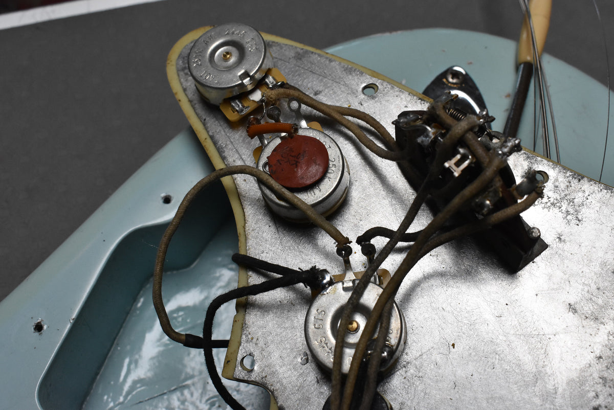 Close-up of the guitar's wiring, showing three pots, a red capacitor, and a switch, all connected by aged cloth-covered wires.