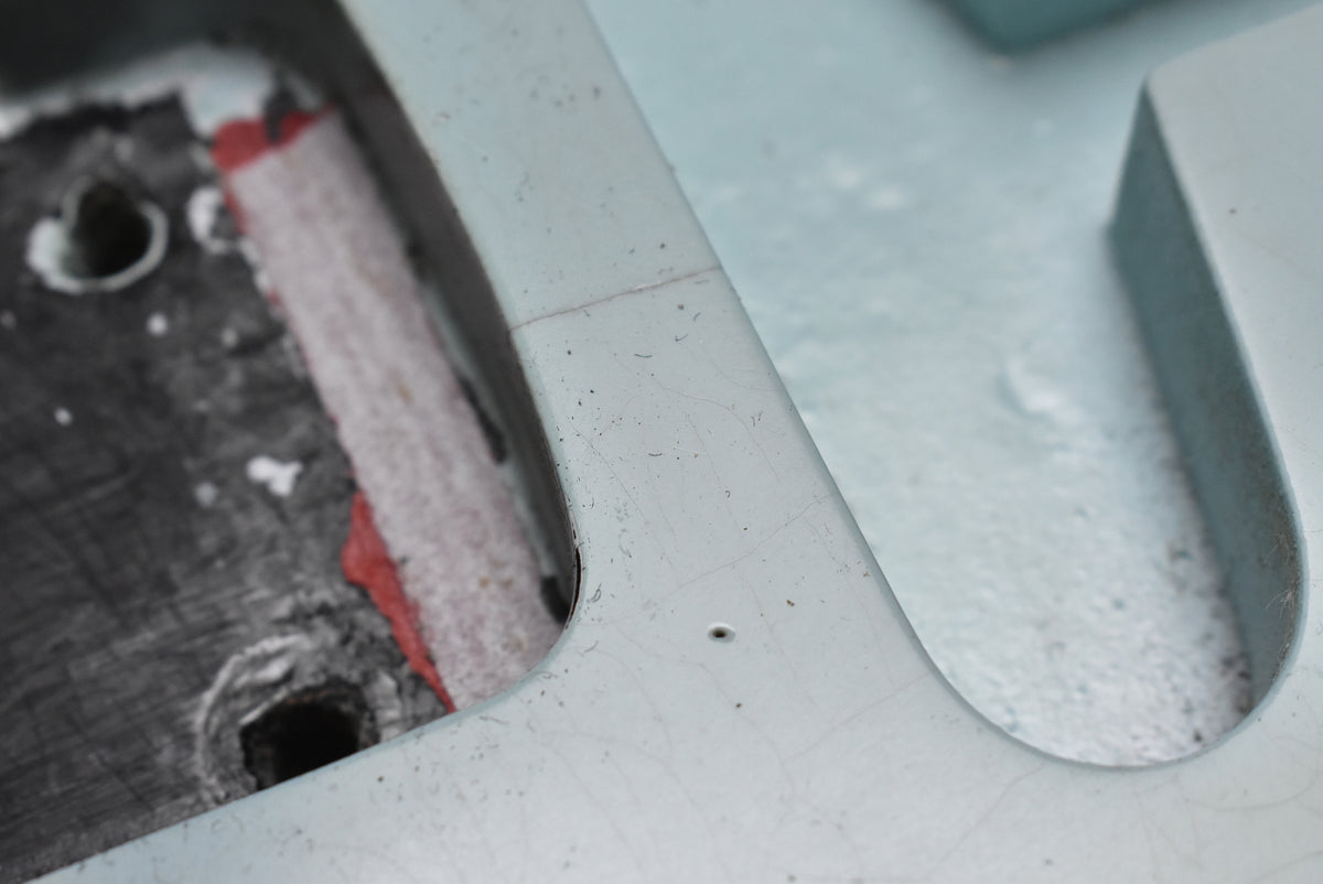 Close-up of the guitar's aged sonic blue finish, showing fine checking, a small screw hole, and a glimpse of red paint in the cavity.