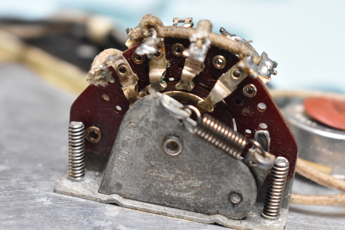 Close-up of the guitar's internal 3-way switch, showing its aged metal casing, springs, and soldered wires on a dark red circuit board.