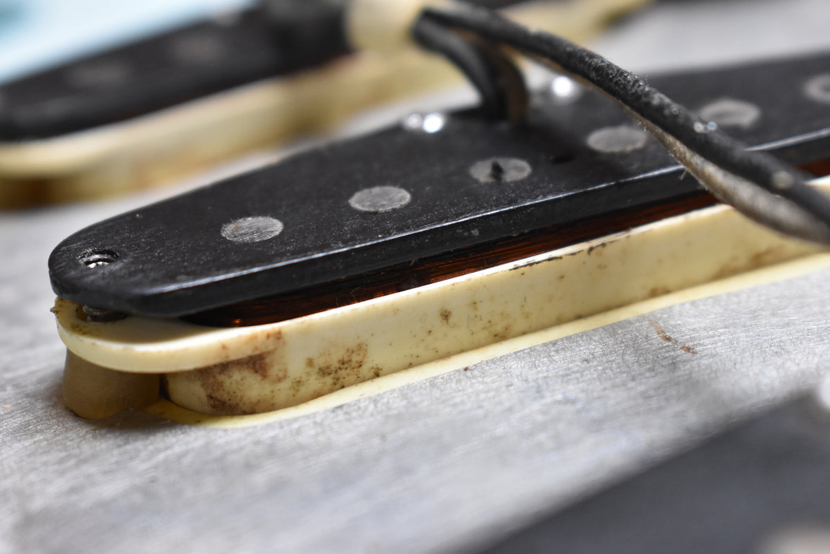 Close-up of a single coil pickup with black cover, exposed copper windings, and aged cream bobbin with visible grime and wear.