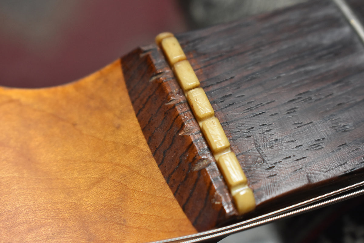 Close-up of the guitar's nut and dark slab board fretboard, showing wear and string grooves on the aged bone nut.